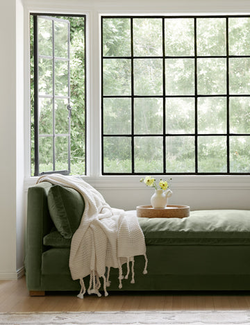 #color::white | The Trestles white chunky knit throw by pom pom at home lays atop sage velvet bench in a nook with a cork tray and white vase