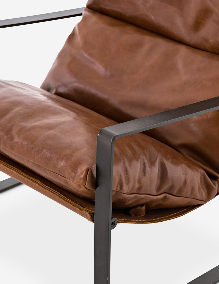 | Close-up of the right metal arm of the brown leather Marlyne sling-back accent chair with black metal frame