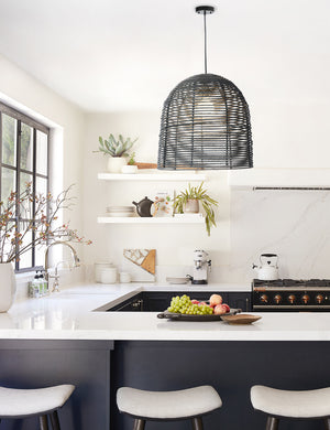 The Beehive black jute woven pendant light is hung above a kitchen island with black cabinetry and white countertops