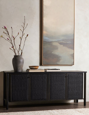 The Isaura black cane-paneled sideboard cabinet styled with a grey vase and a large canvas wall art piece.