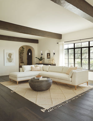 The Charleston ivory left-facing sectional sofa sits in a living room atop a diamond patterned rug next to a circular coffee table