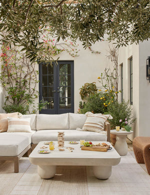 The Clouded square white coffee table sits on a patio atop an ivory rug next to a woven accent chair and sectional sofa