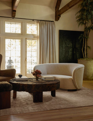 The Chiltern sand dune rug lays in a dark living room under a linen sofa, a round wooden coffee table, and a brown accent chair