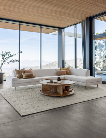#showall::39808547553379 | The Estee white linen right-Facing Sectional Sofa sits atop a textured white rug in a room with floor to ceiling windows