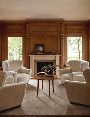 The Chiltern sand dune rug lays in a living room with wooden accented walls under four boucle accent chairs
