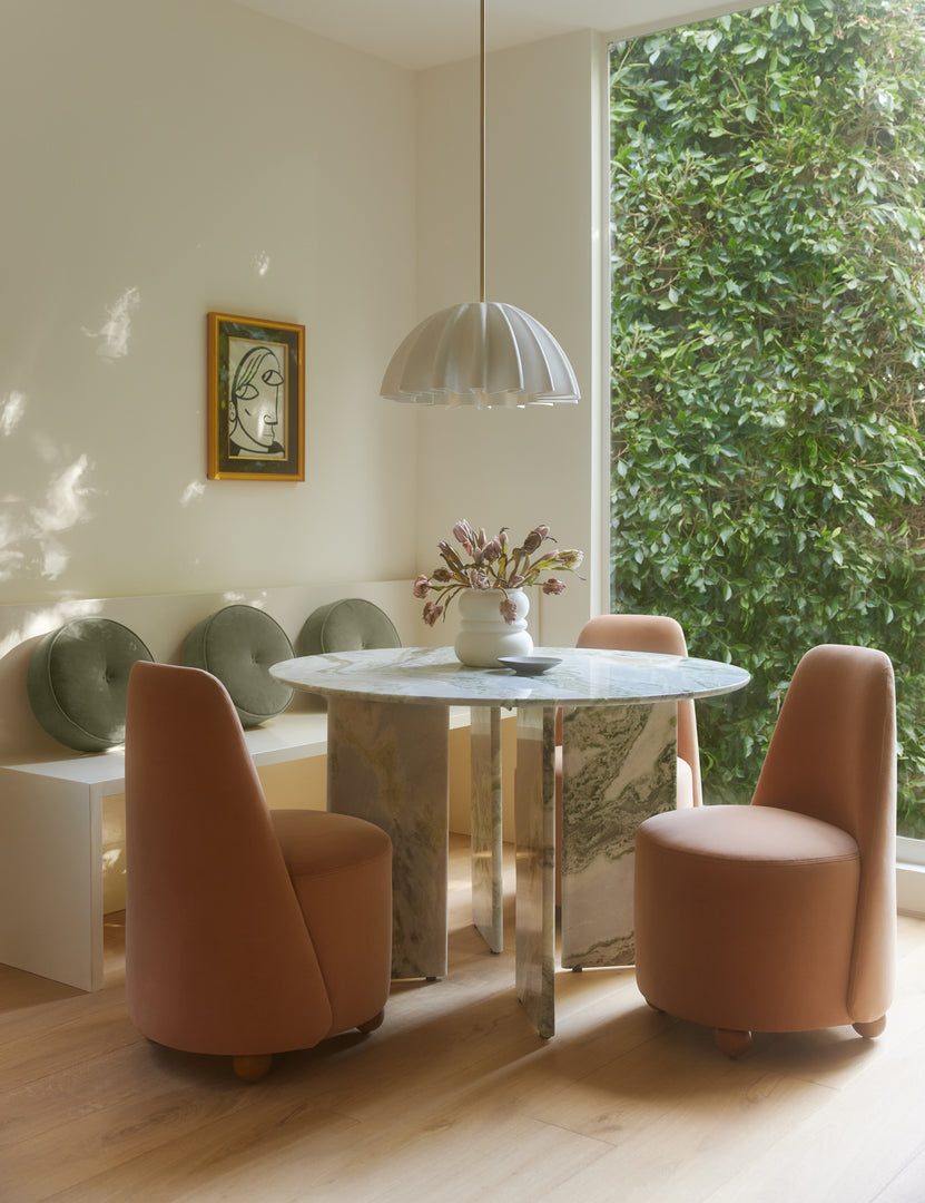 #color::green-onyx-marble | Celia round dining table styled with a ruffled pendant light and three peach colored velvet dining  chairs.