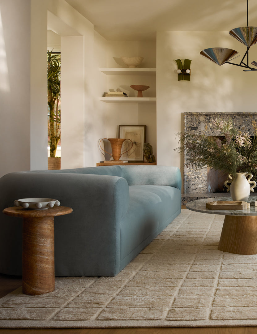 #color::faux-canyon-travertine | Mona round stone drink table styled next to a blue velvet sofa.