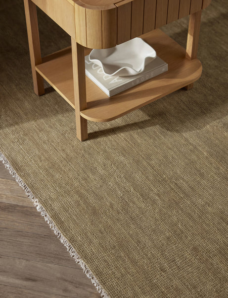 #color::moss-gray #size::2-6--x-8--runner #size::3--x-5- #size::5--x-8- #size::6--x-9- #size::8--x-10- #size::9--x-12- #size::10--x-14- #size::12--x-15- #size::2--x-3-  #size::4--x-6- #size::6--round #size::8--round | The Heritage moss gray rug lays under a rectangular side table with a book and white ruffle bowl in its shelf