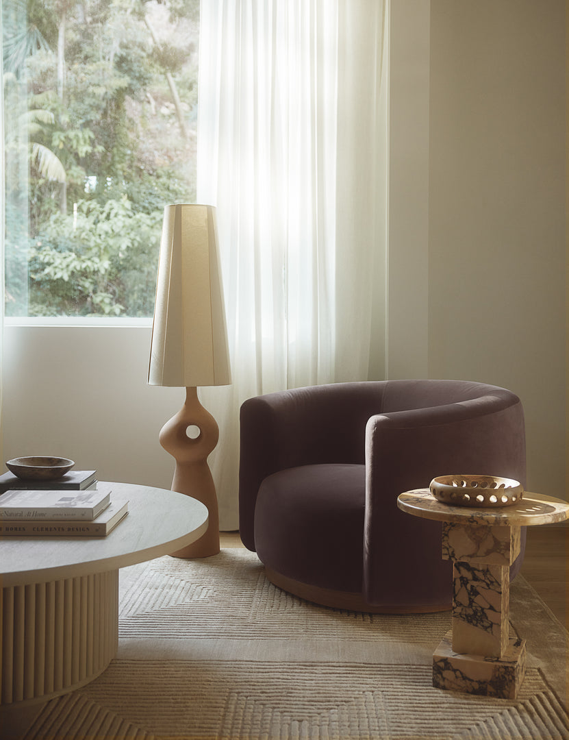 #color::mink-velvet | Lowry rounded silhouette velvet accent chair styled with a round orange marble side table and sculptural floor lamp.