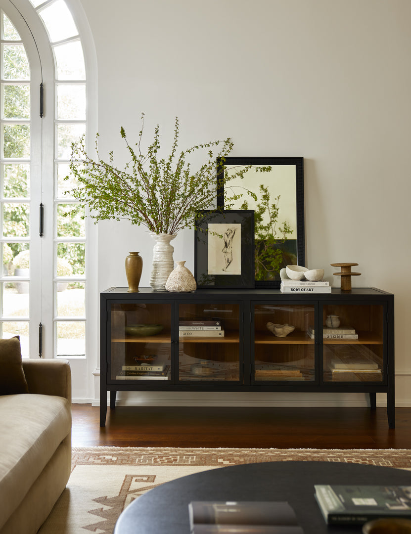 | The Morey glass front black curio sideboard cabinet in a living room with various vases and artwork styled on top