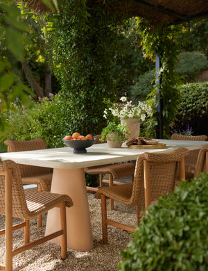 Keating sculptural two-toned outdoor dining table styled with wicker and teak outdoor dining chairs.