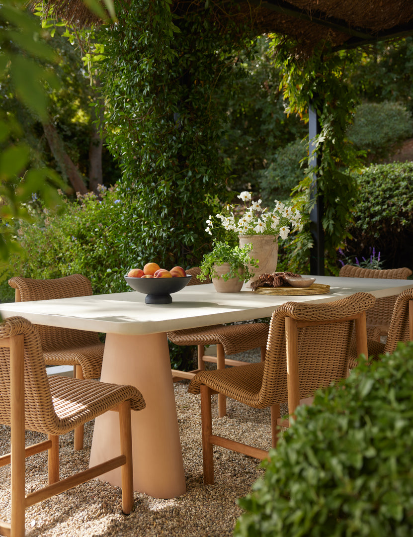 #color::ivory-and-terracotta | Keating sculptural two-toned outdoor dining table styled with wicker and teak outdoor dining chairs.