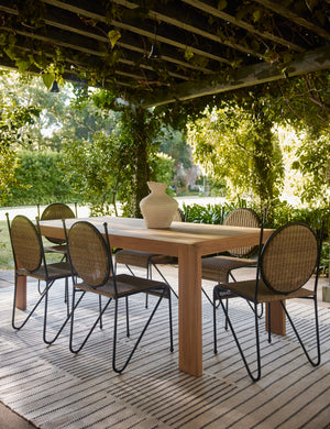 Six Ziggy modern wicker outdoor dining chair by Sarah Sherman Samuel surrounding a teak outdoor dining table under a pergola.