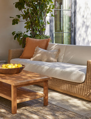 Thorpe outdoor pillow in terracotta and the Thorpe outdoor lumbar pillow in ivory styled on a wicker sofa.