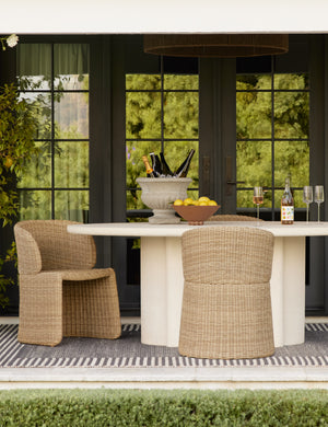 Rodrigo sculptural oval outdoor dining table styled with two wicker outdoor dining chairs.