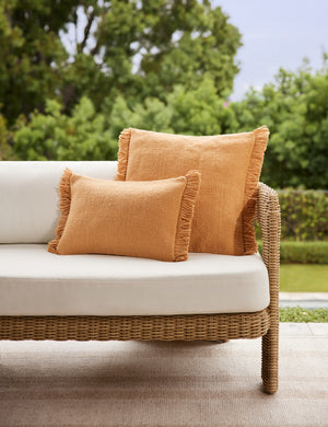 The lumbar and square sizes of the Thorpe outdoor pillow in terracotta styled on a wicker sofa.