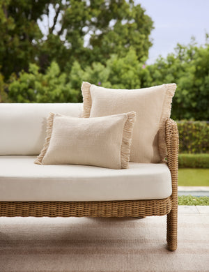 The Thorpe chunky woven fringed ivory outdoor pillow in the square and lumbar sized styled on an outdoor sofa.