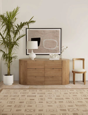 Kono 6-drawer curved oak wide dresser styled as a sideboard decorated with a white table lamp, white ruffle bowl and modern framed artwork.