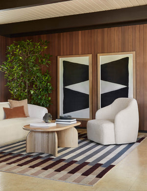  The Tobi cream boucle swivel chair sits atop a striped rug in front of a wood paneled wall with two large geometric wall arts