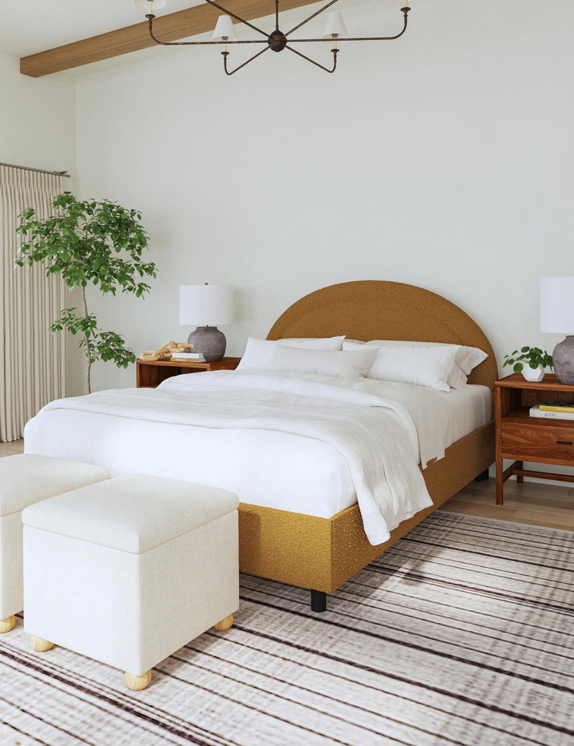 #color::ochre-boucle #size::full #size::queen #size::king #size::cal-king | The Odele ochre boucle platform bed sits atop a striped black and white rug with two ivory linen ottomans sitting at the end