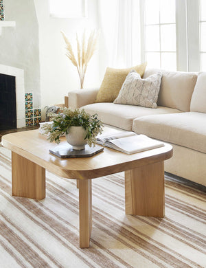 The Manon linen mustard yellow square boucle pillow sits on a natural sofa in a living room with a striped rug and an elevated coffee table