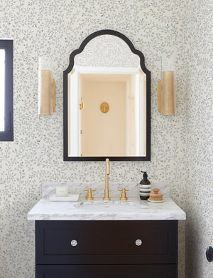 The Dainty Leaves floral Wallpaper by Rylee + Cru is in a bathroom with a black wooden marble topped sink and a black framed arched mirror