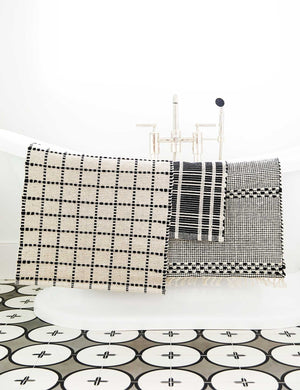 The Sebou natural and black dotted machine washable mat is draped over a white bathtub with other bath mats