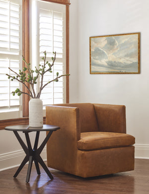 The golden framed Study of Clouds with a Sunset near Rome Wall Art by Simon Alexandre Clement Denis is hung in the corner of a living room with a black wooden side table, a brown leather accent chair, and a white ribbed vase