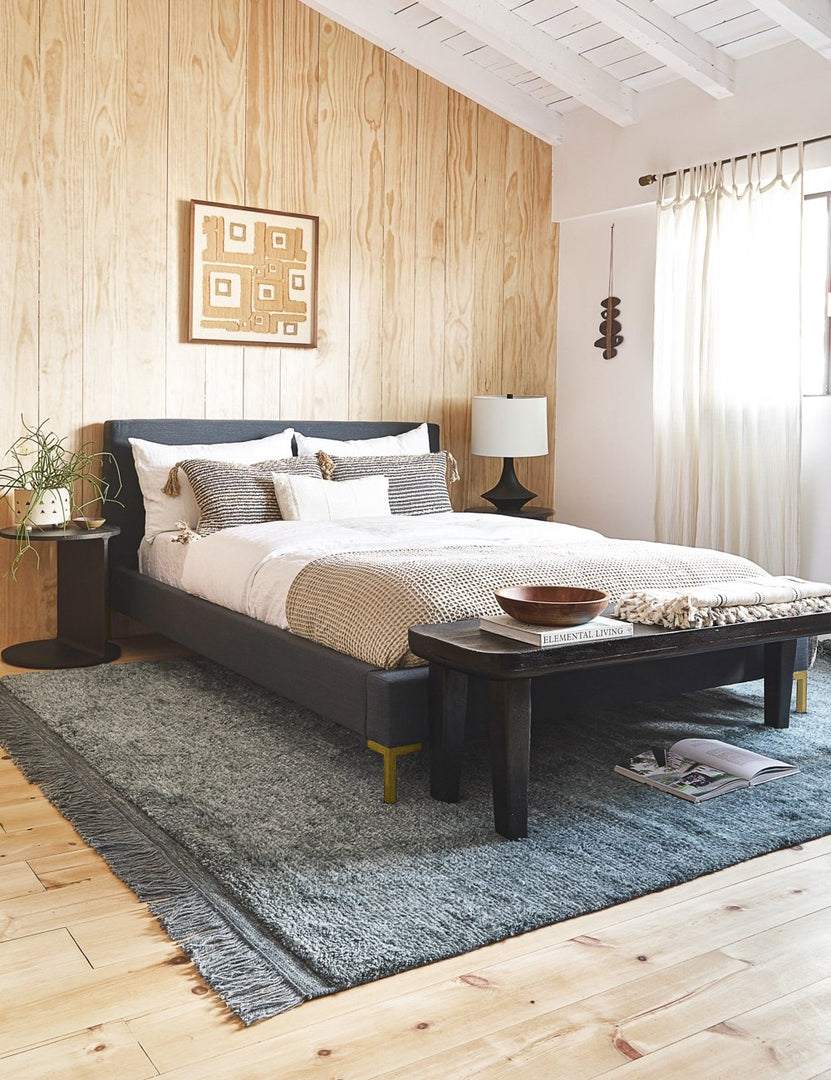 #showall::39559967965283 | The Deva navy linen bed lays in a bedroom with a wooden paneled wall atop a gray fringed rug