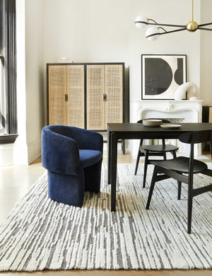The Adeline black and brass retro chandelier sits in a dining room with a black wooden dining table, black wooden dining chairs, and a navy velvet accent chair