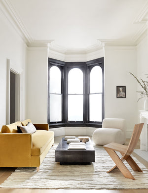 The Peregrine black and white marled striped lumbar pillow lays in a living room with a yellow velvet sofa, floor to ceiling windows, and a wooden accent chair
