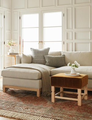  Hollingworth Natural Linen sectional sofa sits in a living room with white accented walls, a cognac velvet ottoman, and a red Persian rug