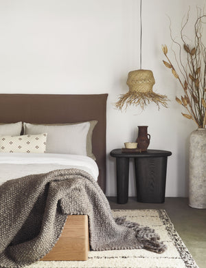 The Harbour Cotton Matelassé taupe Coverlet by Pom Pom at Home with geometric woven texture sits on a brown linen framed bed in a bedroom with a jute pendant light and a sculptural black nightstand