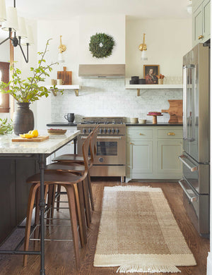 The Joelle rust rug in its runner size lays in a kitchen with white and black countertops, bar stools, and stainless steel appliances