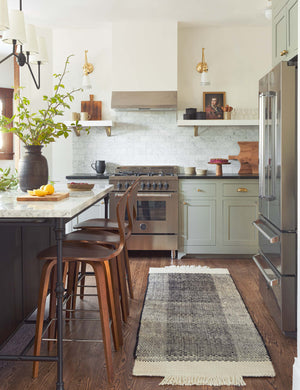 The Joelle black rug in its runner size lays in a kitchen with white and black countertops, bar stools, and stainless steel appliances