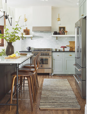 The Khloe gray rug in its runner size lays in a kitchen with white and black countertops, bar stools, and stainless steel appliances