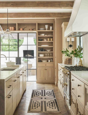 The Senna neutral hand-knotted wool area rug with black geometric pattern sits in a light wood kitchen.