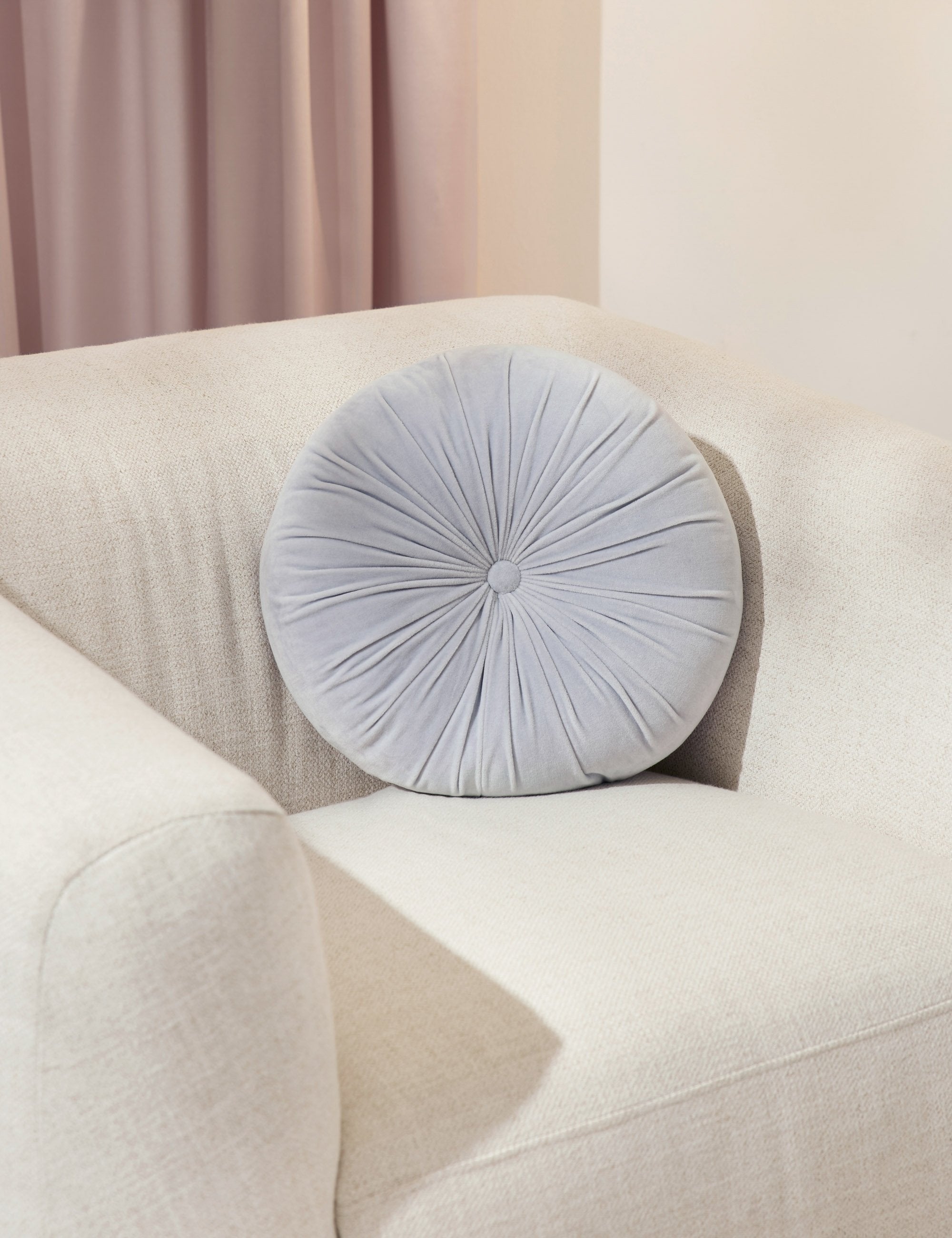 The Monroe ice blue velvet round pillow sits on a white accent chair