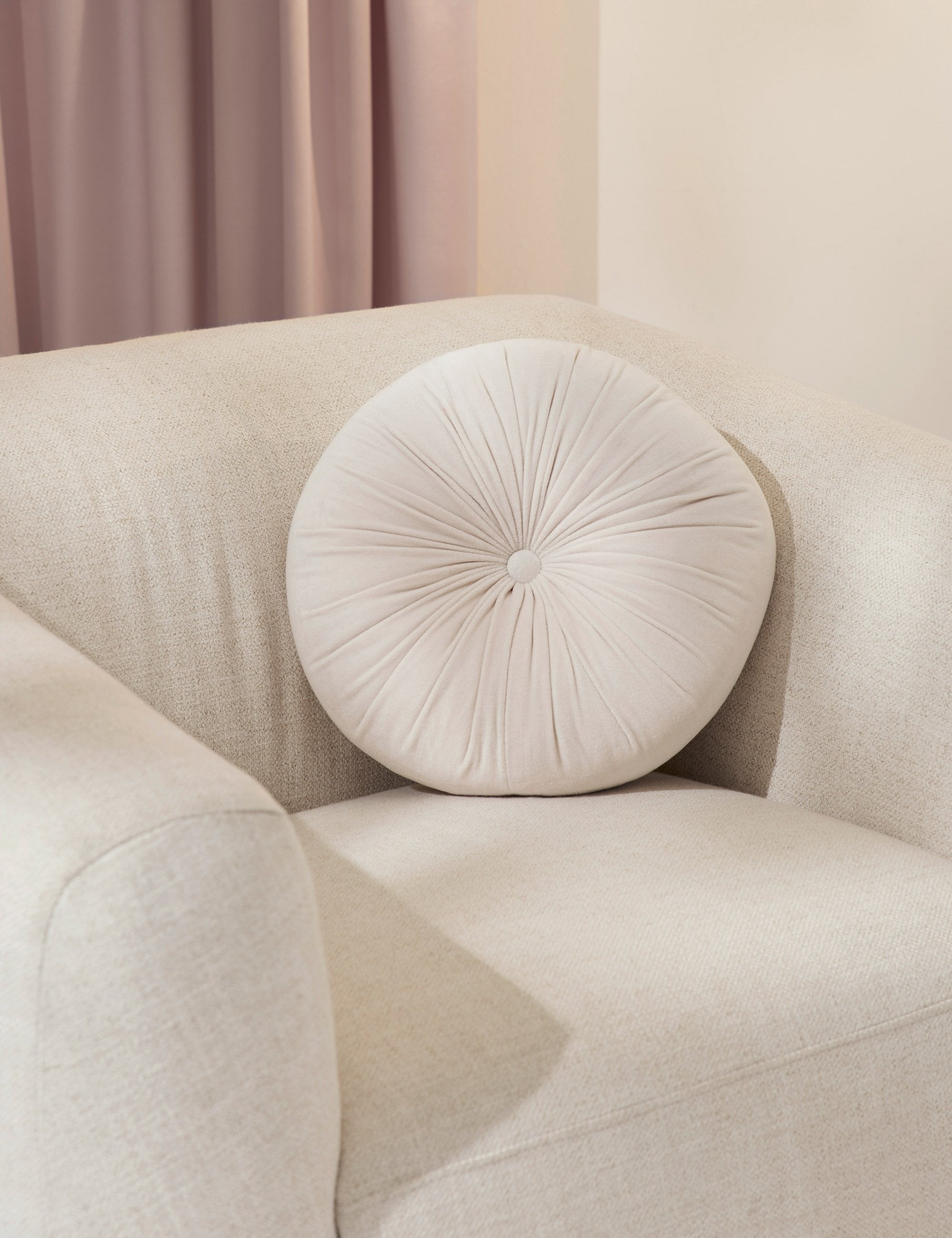 The Monroe oyster white velvet round pillow sits on a white accent chair