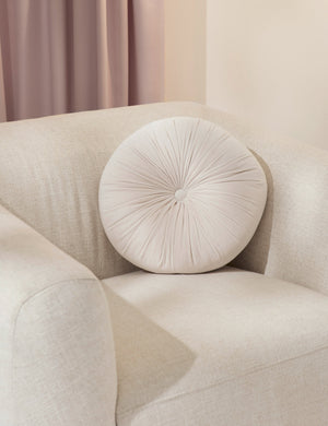 The Monroe oyster white velvet round pillow sits on a white accent chair