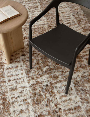 The Tegan Moroccan Shag Rug lays under a circular light wooden side table and a black dining chair