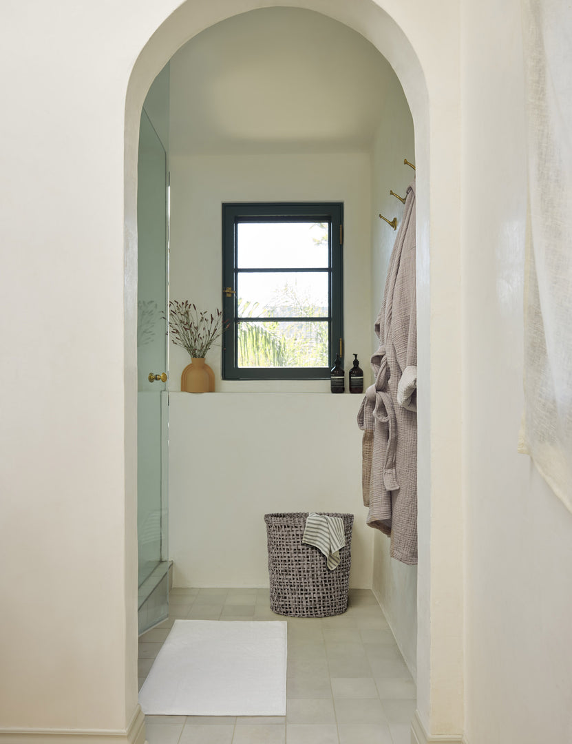 #color::white | The Cloud loom sustainable bath mat by coyuchi lays on a white tiled floor in a bathroom with an arched entryway