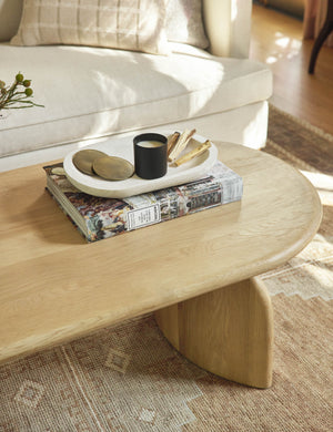 The Clemente whitewashed paulownia wood bowl sits in a living room atop a light wood coffee table with a stack of books and a candle