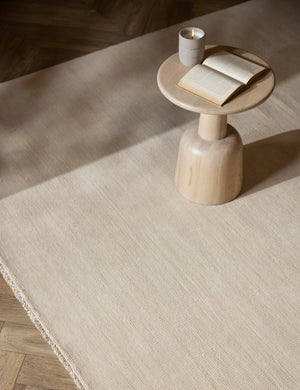 The Heritage ivory rug lays under a light wooden round side table with a lit candle and open book atop it