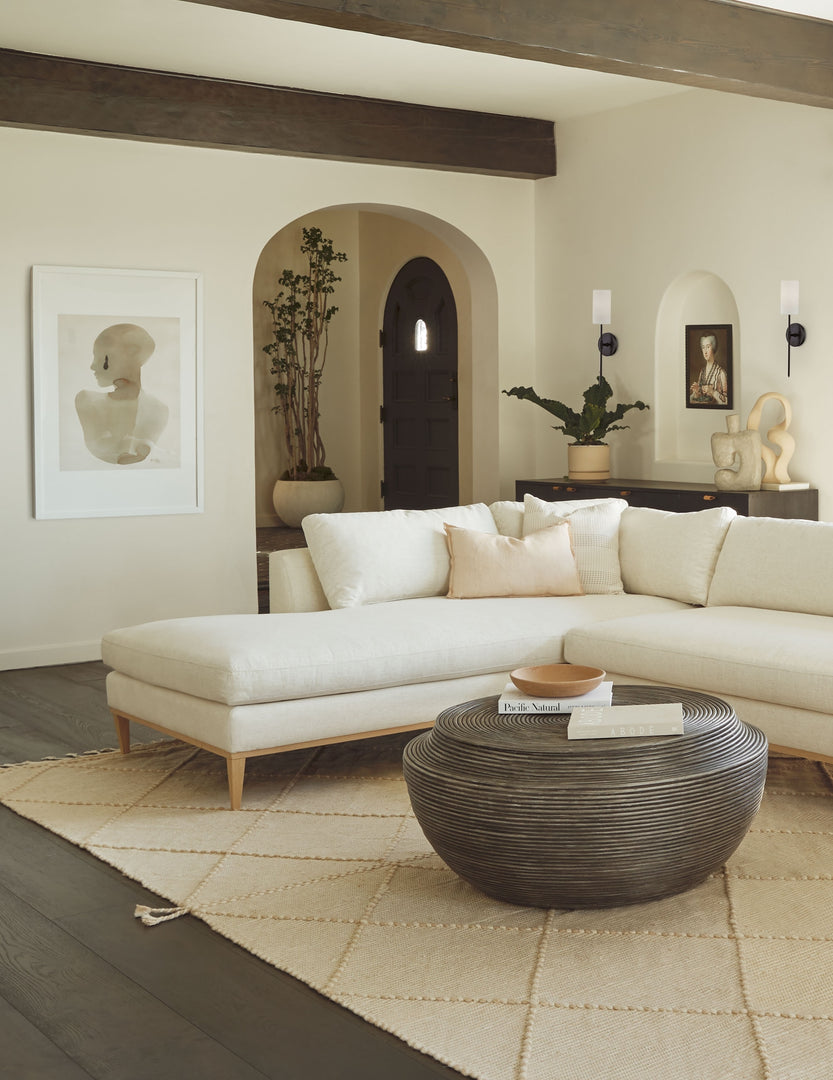 #color::white #size::3225--x-4725- #size::3825--x-5625- | The Sara singh back drop portrait neutral toned wall art by Stampa is hung in a living room with a white linen sectional sofa, a round wooden coffee table, and a textured beige rug