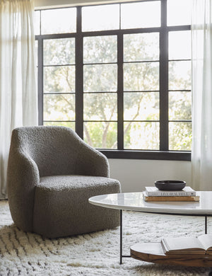  The Tobi gray boucle swivel chair sits atop a plush ivory rug in front of a wall with large black-framed windows and sheet curtains