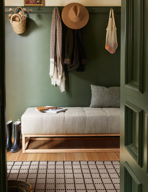 The Sebou natural and black dotted machine washable mat lays in a green entry way with a gray linen cushioned bench