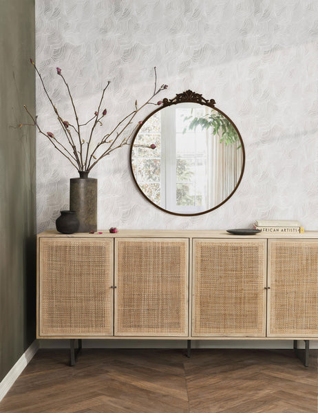 #color::oil-rubbed-bronze | The tulca oil rubbed bronze round mirror hands on a wall above a rattan sideboard next to a brown vase