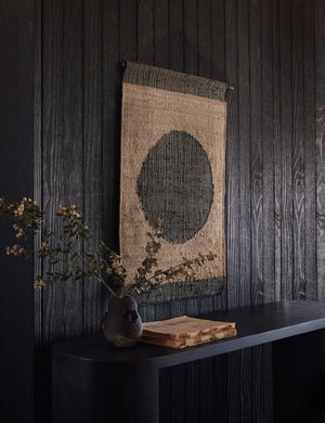 Katlee black and natural flat weave Wall Hanging with circle in the center hangs on a black wooden wall above a black console table