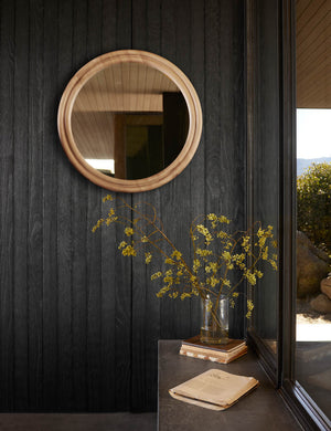 The Bourdon Double-Framed Natural Ash Round Mirror hangs on a black wood paneled wall